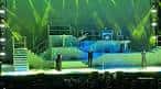 Interior del auditorio con escenario iluminado en tonos verdes durante un espectáculo