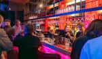 Barra de bar iluminada con luces de neón, mostrando el ambiente social del local