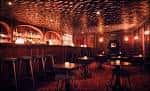 Interior de un bar o sala de eventos con iluminación cálida, barra y mesas