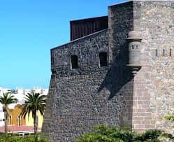 Detalle de la torre del castillo con almenas y muros de piedra bajo cielo azul