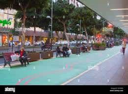 Avenida peatonal con bancos, vegetación y personas caminando bajo techo