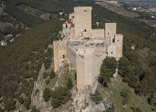 Vista aérea del castillo en su entorno natural, rodeado de vegetación y montañas