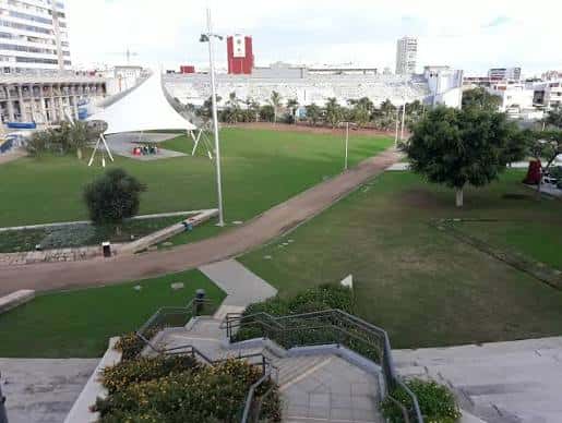 Vista elevada del parque con zona de juegos, senderos y el estadio Insular en el fondo