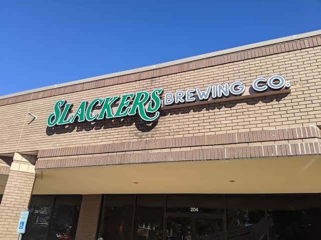 Fachada exterior de Slackers Brewing Co. con letrero verde sobre ladrillo