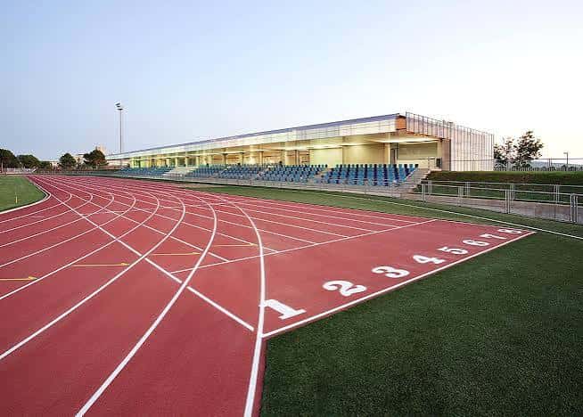 Vista general de la pista de atletismo con gradas y edificio moderno al atardecer
