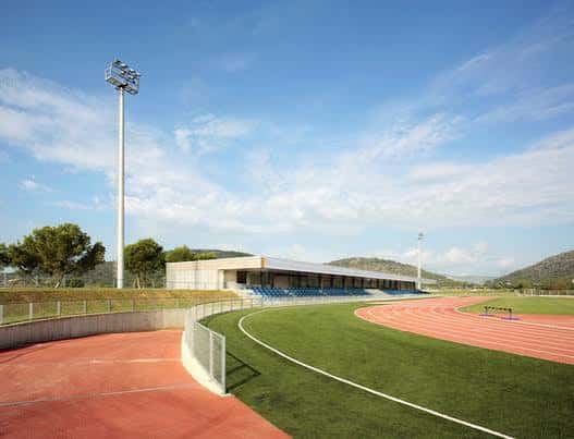 Pista de atletismo rodeada de césped con torres de iluminación y montañas al fondo