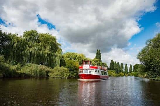 Barco de City Cruises navegando por el río Ouse rodeado de árboles verdes y cielo nublado