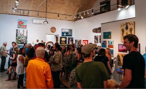 Interior del espacio mostrando una exposición de arte con público asistiendo a la inauguración