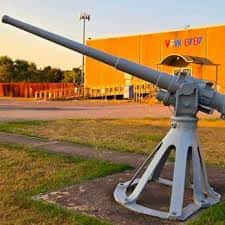 Cañón histórico en el exterior del VFW Post 8787 con fachada amarilla al atardecer