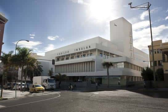 Ángulo amplio del edificio blanco del Cabildo con sol brillante y vehículos en primer plano