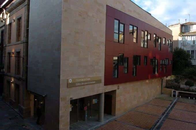 Fachada lateral del edificio universitario con detalles arquitectónicos en piedra y panel rojo