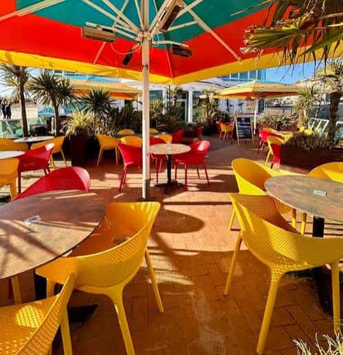 Terraza exterior del establecimiento con mesas coloridas y sombrillas bajo el sol