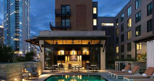 Área de piscina al atardecer con bar iluminado y vistas a la ciudad