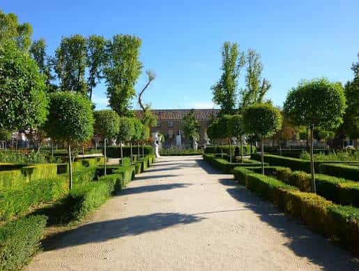 Paseo central del Jardín de Isabel II con setos y árboles enmarcando la vista hacia el palacio