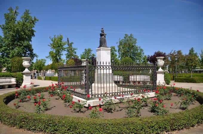 Monumento a Isabel II rodeado de flores rojas y jarrones ornamentales en el jardín