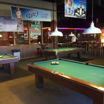 Vista del área de juego con tablas de billar y barra en el fondo