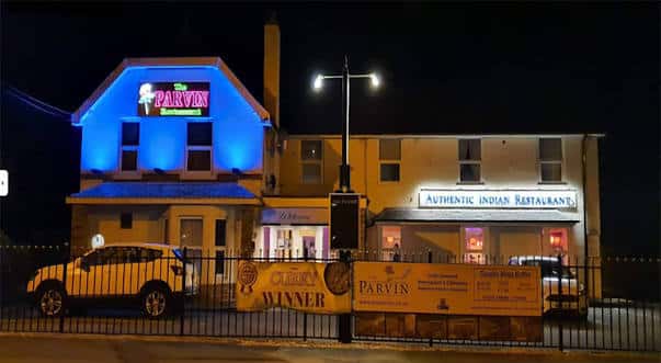 Fachada exterior nocturna del restaurante The Parvin con iluminación azul y letrero luminoso