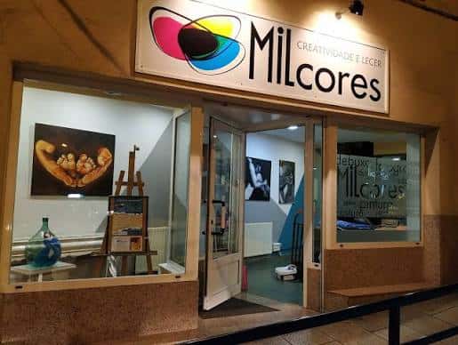 Fachada nocturna de Mil Cores con letrero iluminado y escaparate mostrando obras de arte