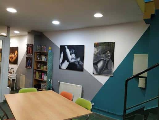 Interior del espacio cultural con mesas, sillas coloridas y cuadros colgados en paredes decoradas
