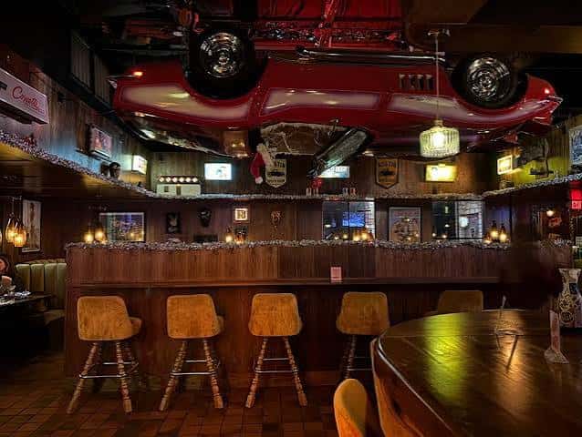 Interior del bar con barra de madera, taburetes y un coche rojo colgado del techo como decoración