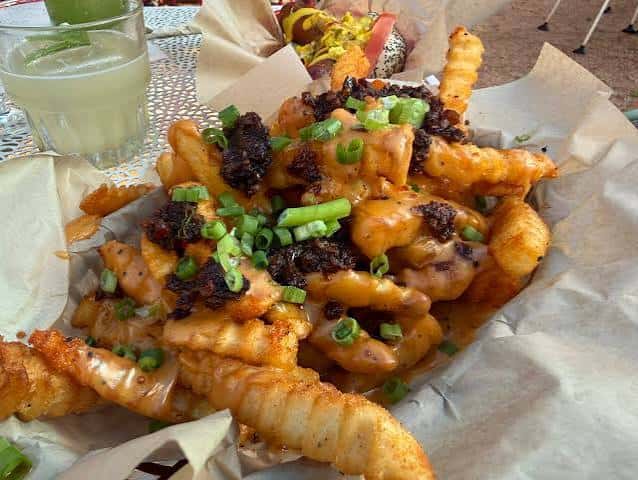 Plato de papas fritas cargadas con queso, cebollín y trozos crujientes
