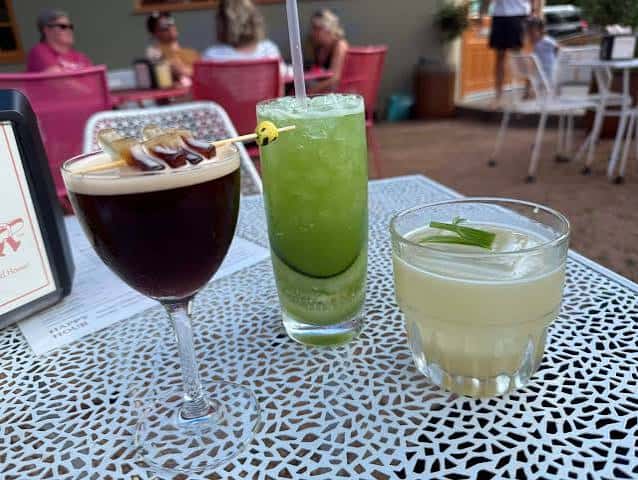 Tres cócteles servidos en una mesa al aire libre con clientes en el fondo