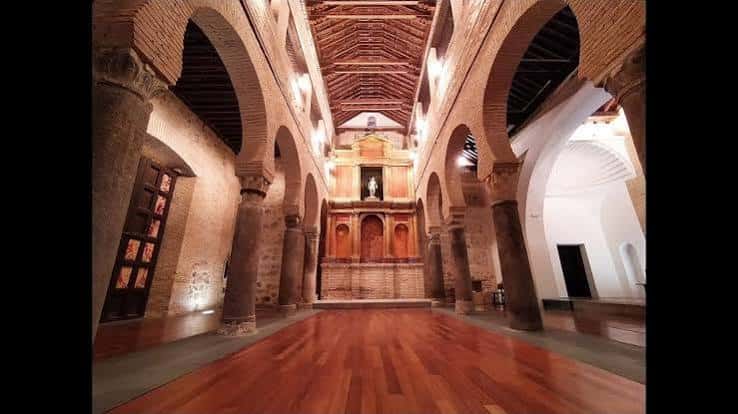 Interior de la iglesia con bóvedas de ladrillo, columnas y altar principal iluminado