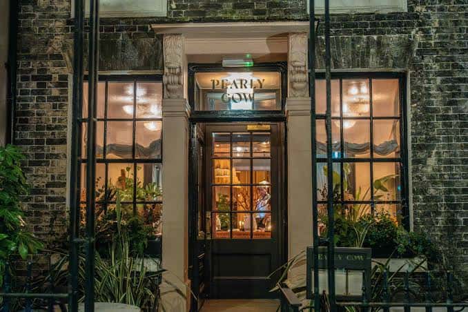 Fachada nocturna del restaurante Pearly Cow con iluminación cálida y detalles arquitectónicos