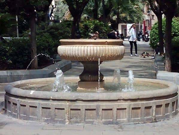 Detalle de la fuente con personas paseando al fondo