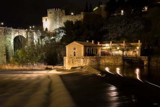 Vista nocturna del Molino de Santa Ana iluminado junto al río y el puente