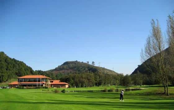 Vista frontal del edificio principal del golf con montañas al fondo en un día soleado