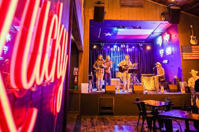 Concierto en vivo en el escenario interior con banda tocando bajo luces de neón