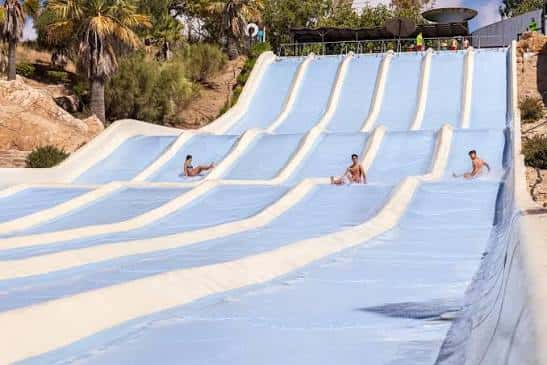 Tobogán múltiple azul con visitantes deslizándose bajo el sol en Aqualand Bahía de Cádiz