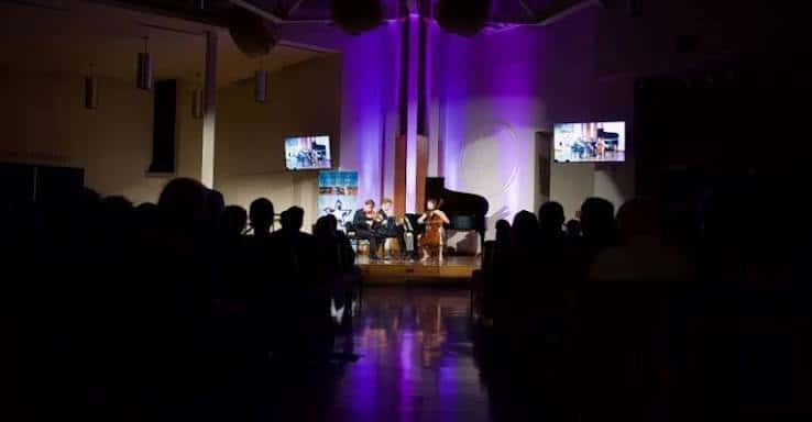 Concierto en vivo con músicos en el escenario bajo iluminación púrpura