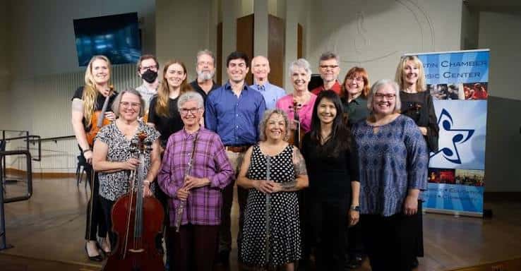 Grupo de músicos y personal posando frente al banner del Austin Chamber Music Center