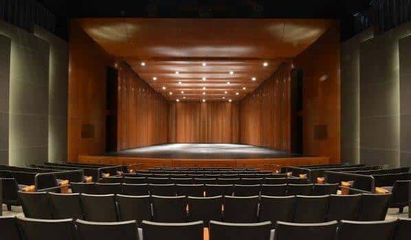Vista interior del teatro desde las butacas hacia el escenario con revestimiento de madera
