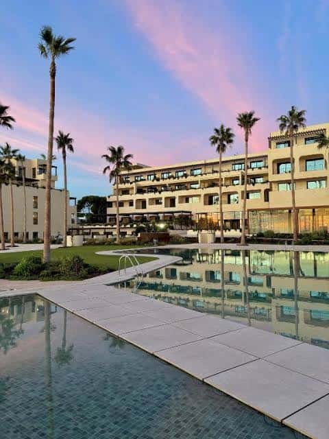 Piscina del hotel al atardecer con palmeras y reflejos en el agua
