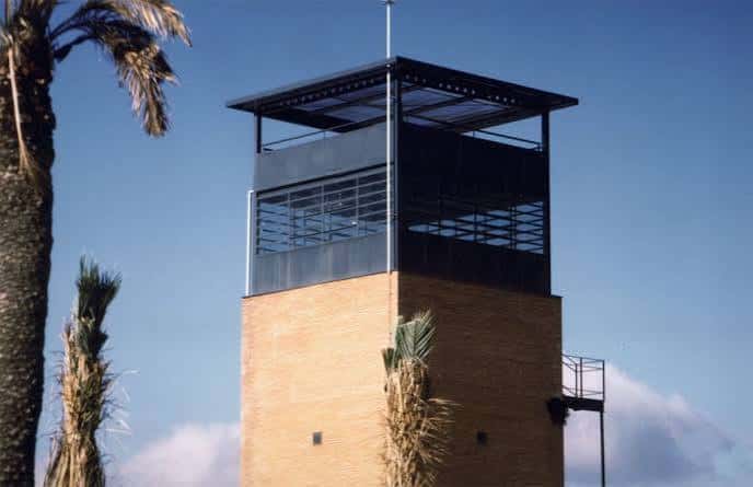 Torre de vigilancia del Centro Penitenciario de Jaén con cielo azul y palmeras