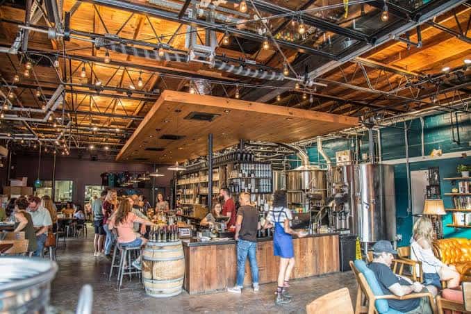 Interior del pub con barra central, techos altos industriales y clientes disfrutando bebidas