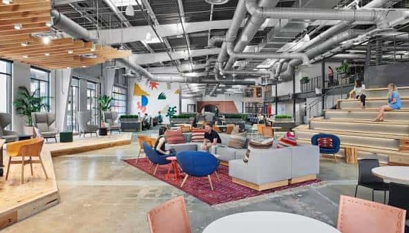 Espacio de coworking moderno con mobiliario colorido y techos industriales