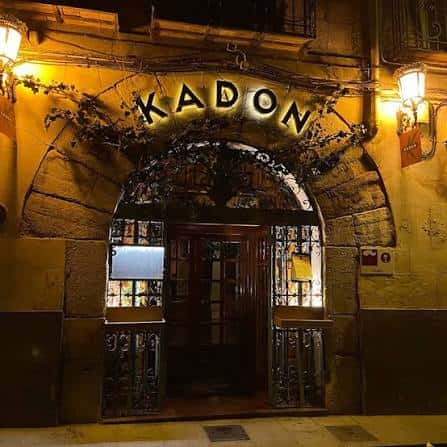 Fachada nocturna del local Kadon con letrero iluminado y arco de piedra