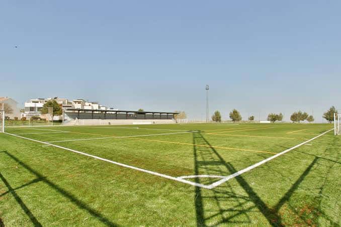 Campo de fútbol con césped artificial y gradas al fondo bajo un cielo despejado