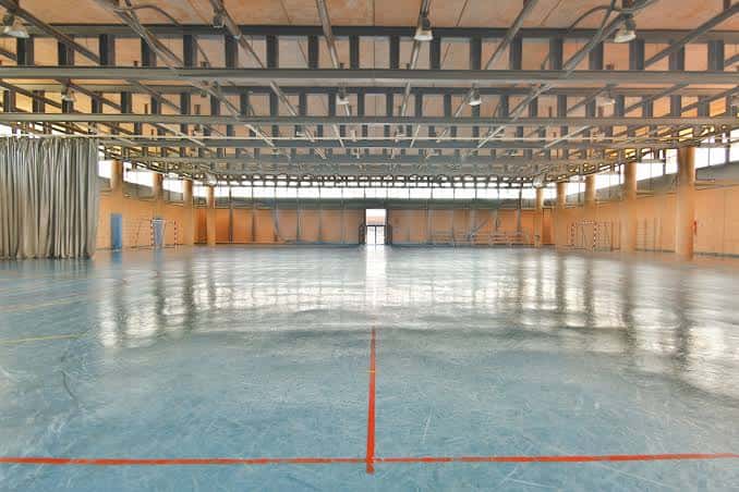 Pabellón deportivo interior con suelo pulido y estructura metálica en el techo
