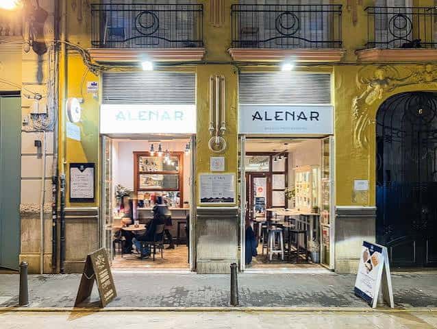 Fachada nocturna de Alenar Bodega Mediterránea con iluminación cálida y clientes en el interior