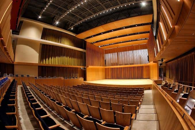 Vista general del interior del auditorio con butacas de madera y escenario iluminado