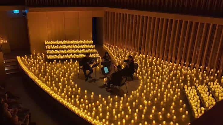 Concierto íntimo en el hall con velas decorando el suelo y músicos en escena