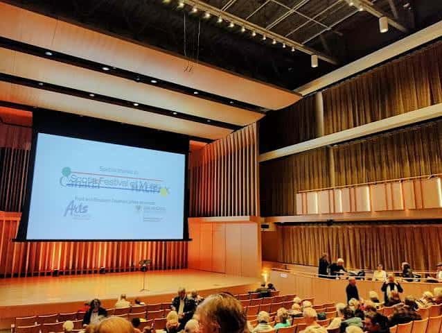 Evento cultural en el Joseph Strug Concert Hall con proyección en pantalla y público presente