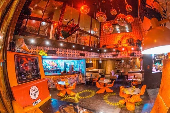 Espacio amplio con mobiliario naranja, espejos y lámparas decorativas