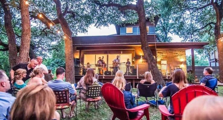 Concierto al aire libre en el porche de Peggy's Porch Party con público sentado y banda tocando bajo luces de cuerda