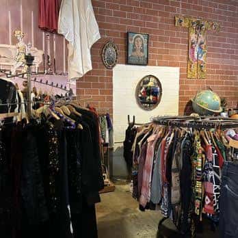 Interior del local con percheros de ropa vintage y decoración ecléctica en pared de ladrillo